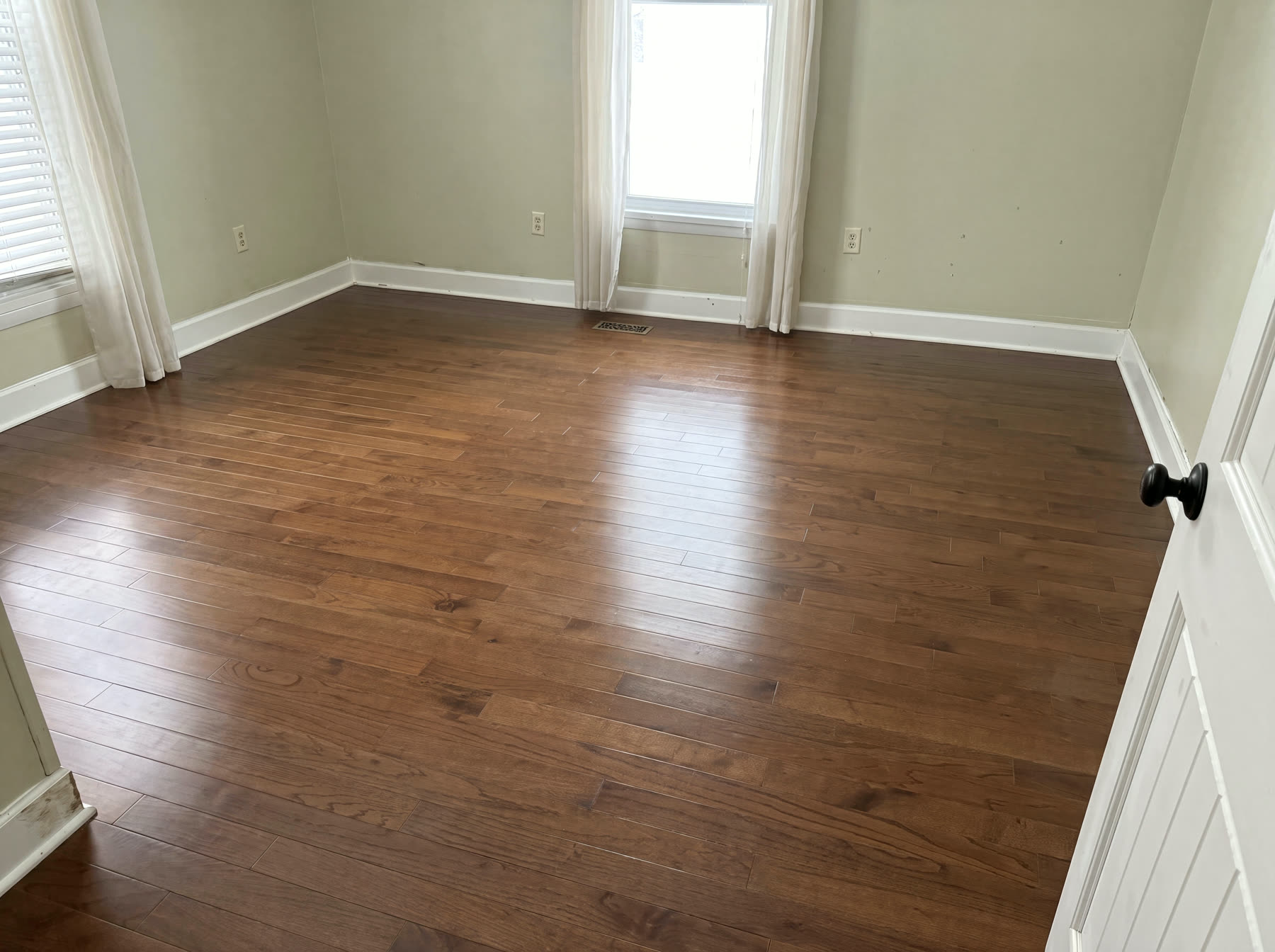 Restored bedroom with new dark-stained hardwood floors and white baseboards