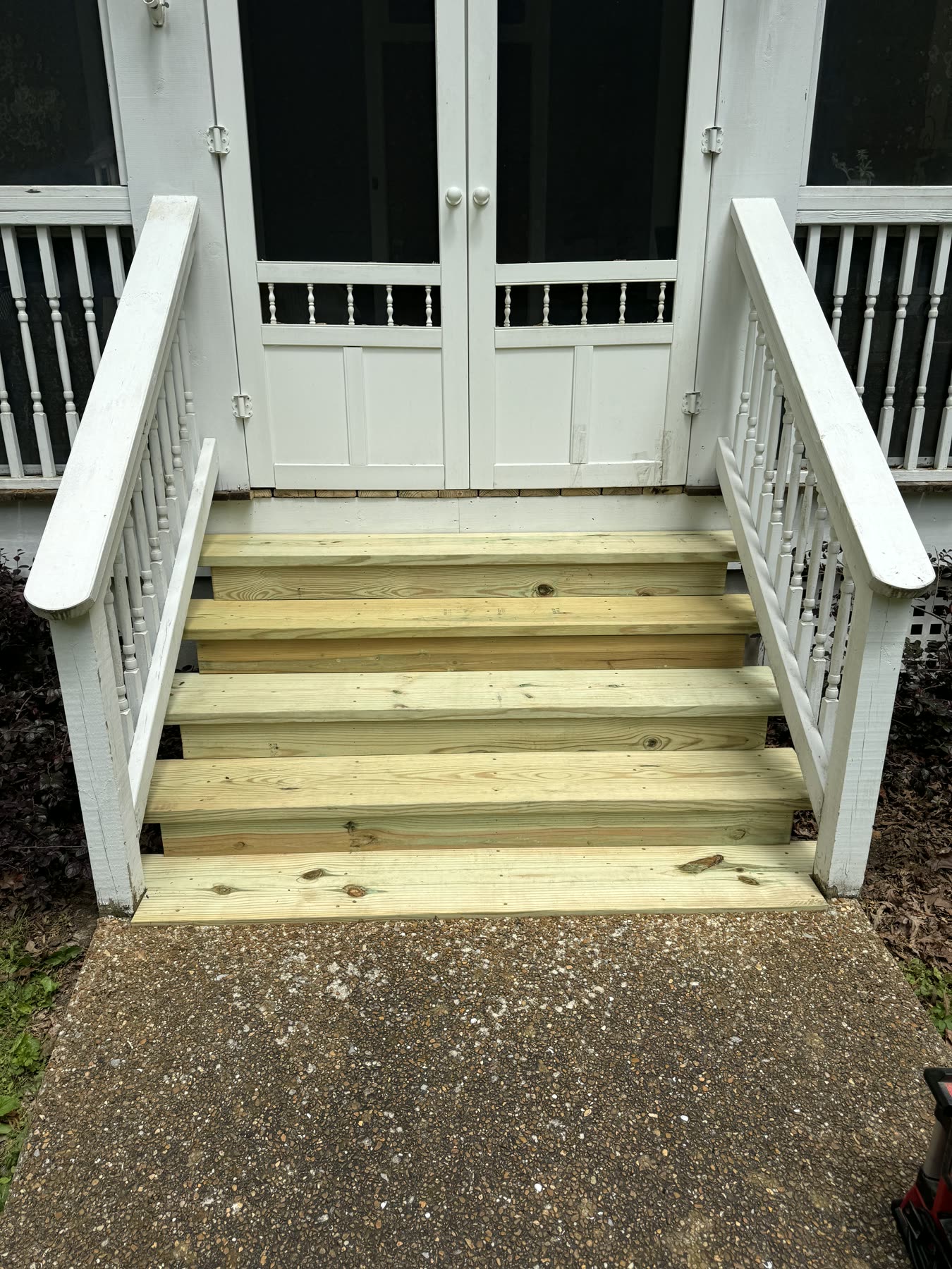 New pressure-treated wood entrance steps between white turned-spindle porch railings