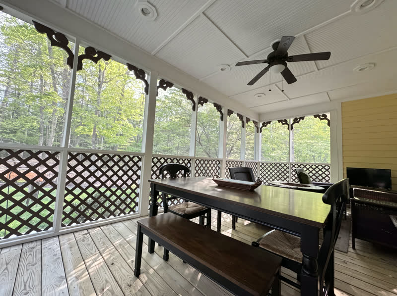 Screened porch with hand-cut dark-wood scroll brackets and white beadboard ceiling on a wooded hillside