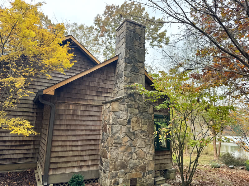 Cedar-shake sided mountain home with dry-stacked fieldstone chimney in fall foliage