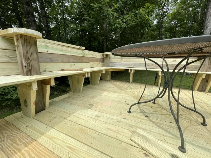 Custom wrap-around built-in deck bench with dark-stained backrest on a rebuilt cabin deck