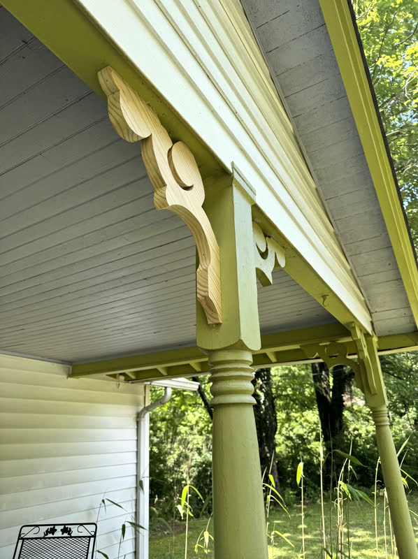 Scroll-cut Victorian gingerbread corbel brackets and turned columns on a restored green cottage porch